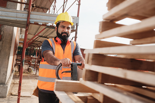 Skilled people working in construction site. Hispanic man at work in new housing project. Professional latino worker using manual pallet jack to move material.